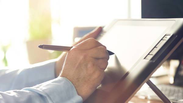 Hand mit Stift zeichnet auf Grafiktablett.