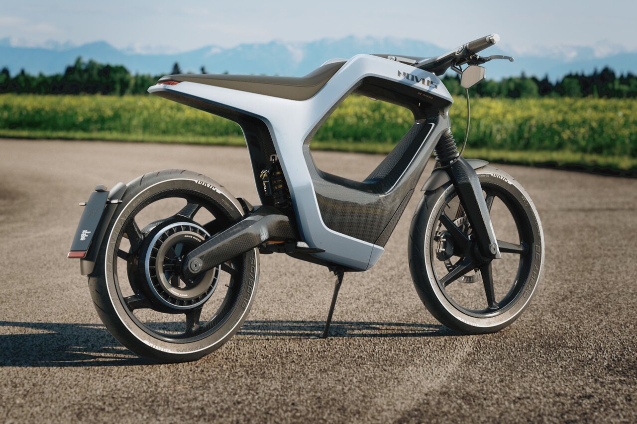 E-Bike mit weißem Rahmen steht auf einer Straße mit Wiese und Alpen im Hintergrund.