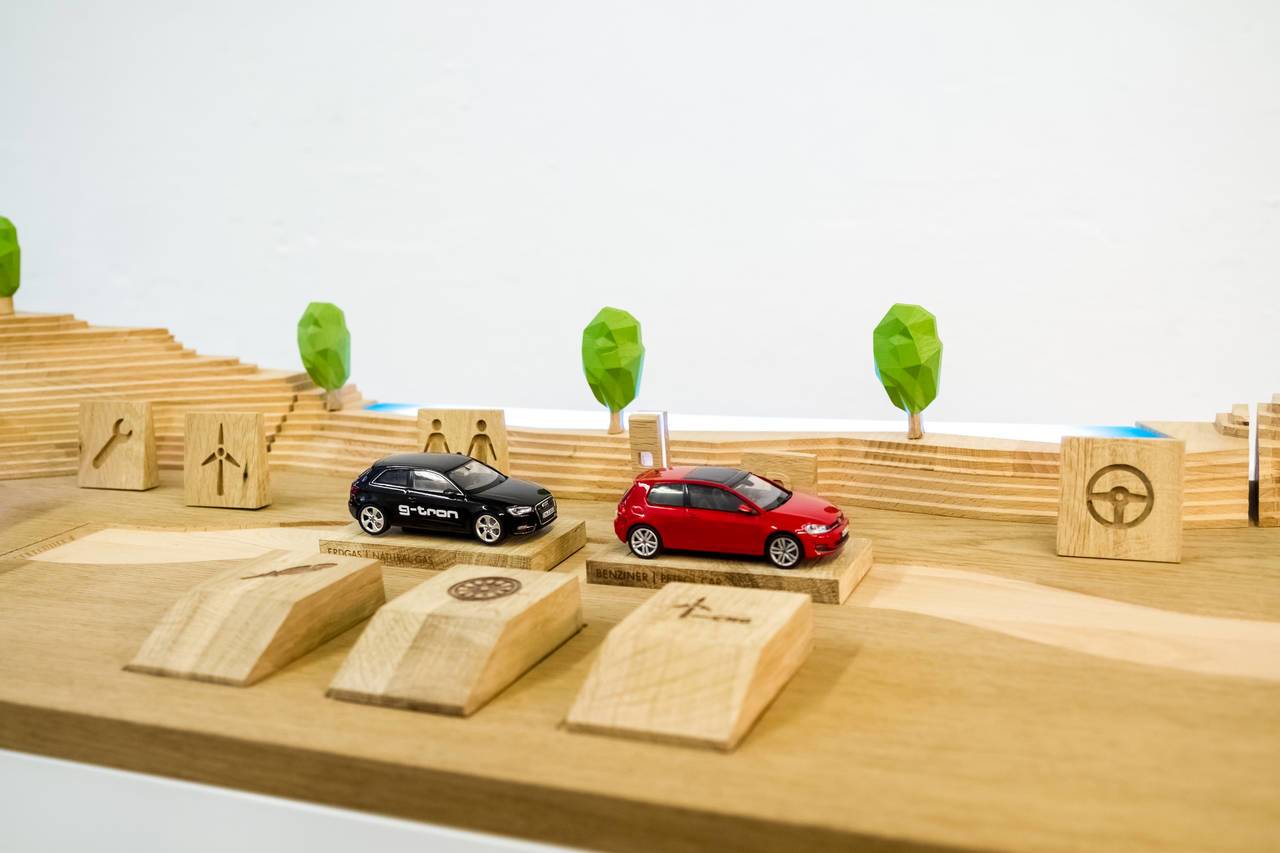 Zwei Modellautos auf Holzplatte mit Symbolklötzen und stilisierten Bäumen.