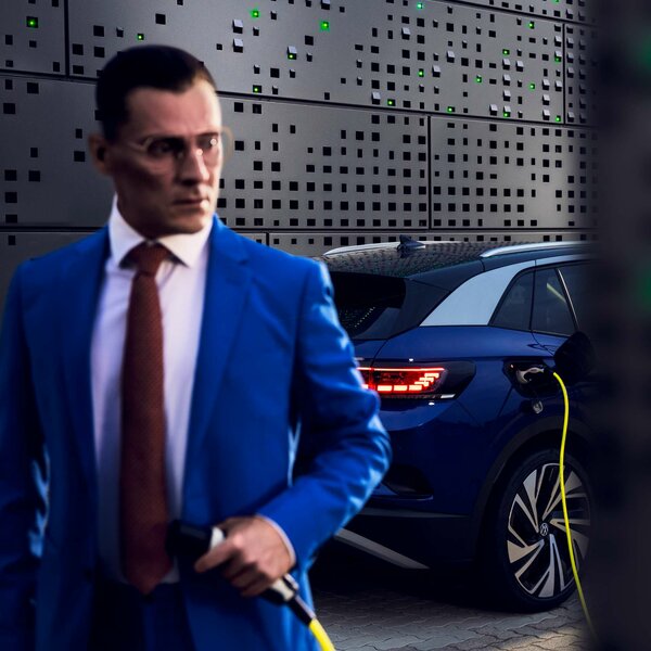 Mann im blauen Anzug mit Ladekabel, E-Auto wird geladen im Hintergrund.