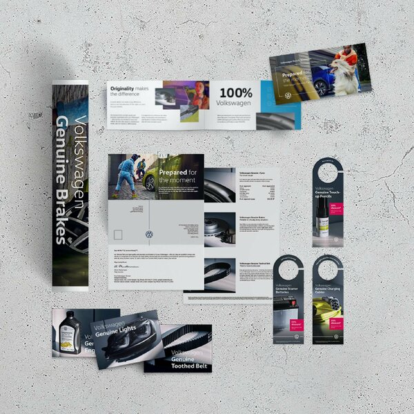 Verschiedene Volkswagen-Marketingmaterialien zu Ersatzteilen und Services auf Betonhintergrund arrangiert.