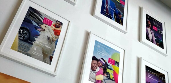 Bilderrahmen mit VW-Werbemotiven hängen an einer weißen Wand.