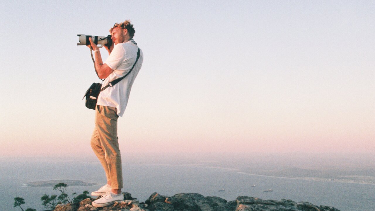 Mann mit Kamera fotografiert von einem Felsen aus die Landschaft bei Sonnenuntergang.