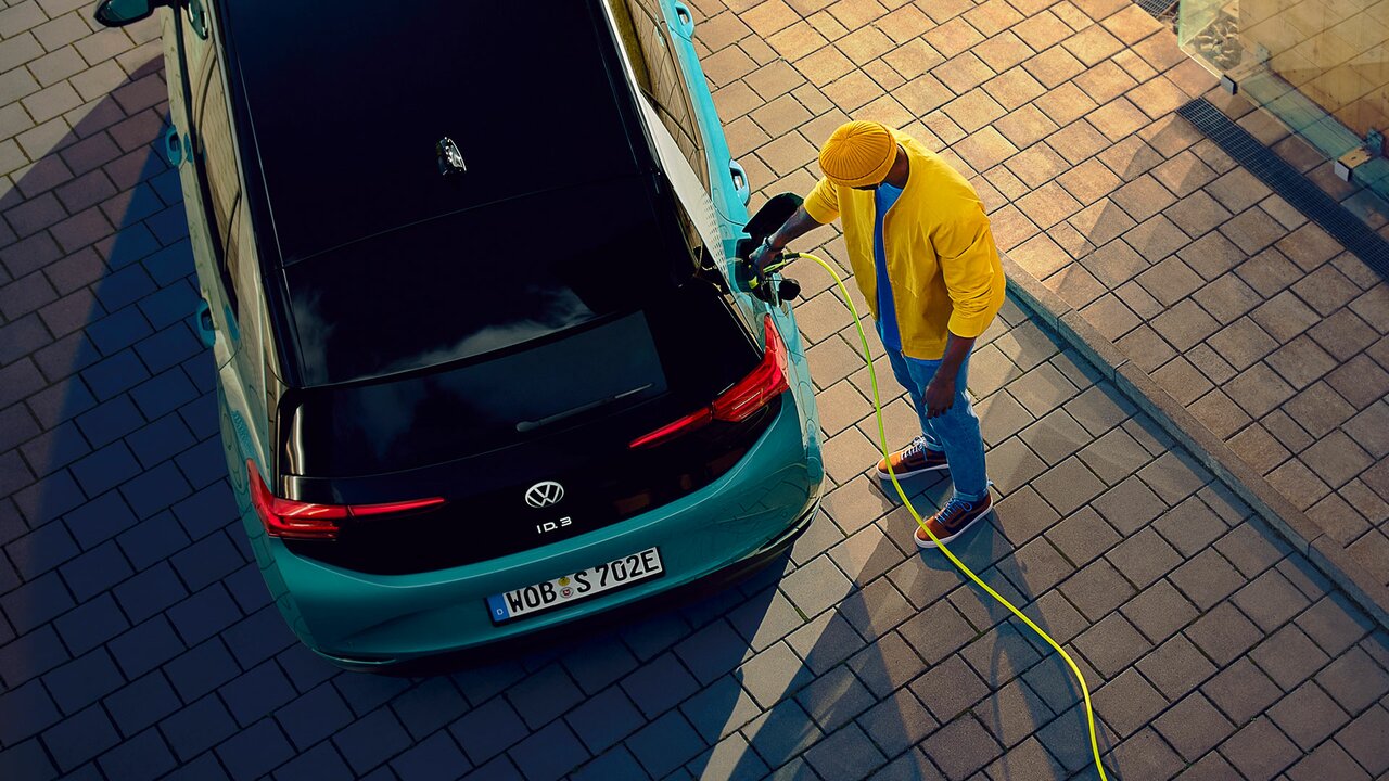 Mann lädt einen türkisfarbenen VW ID.3 mit gelbem Ladekabel an einer Hauswand.