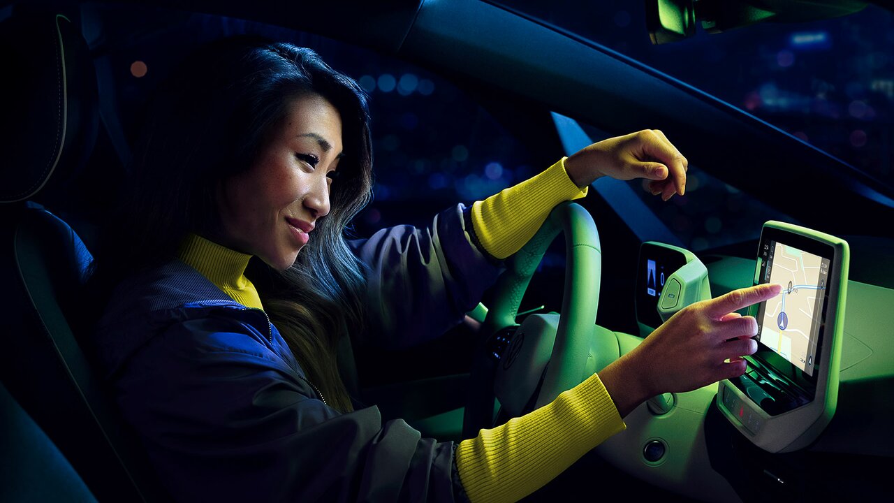 Frau sitzt nachts im Auto und tippt auf das Navigationsdisplay.