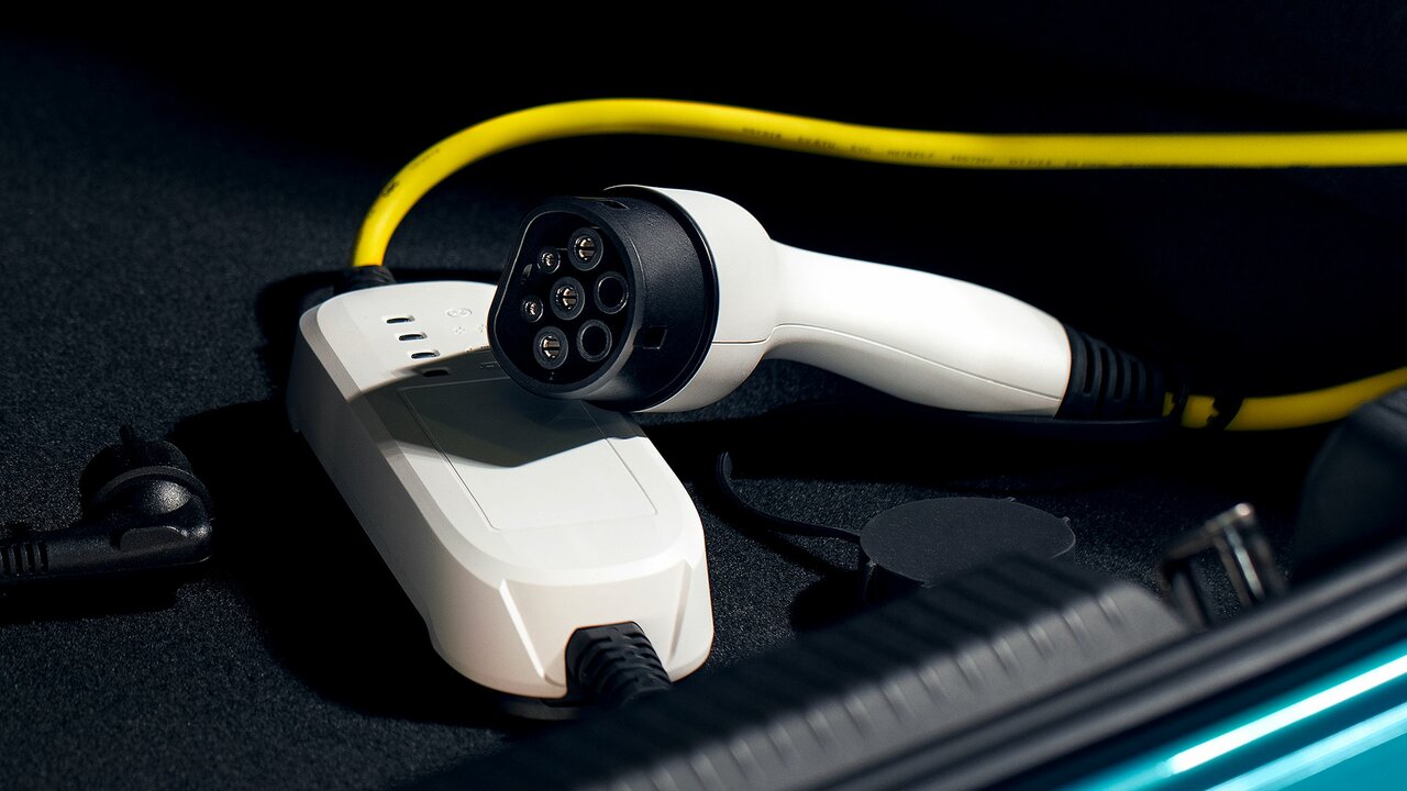 Weißes Ladekabel mit Stecker liegt neben einer Ladeeinheit im Kofferraum.