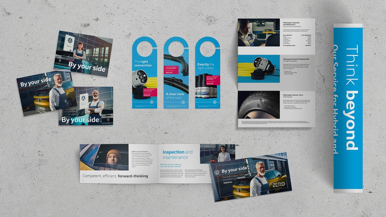 Diverse VW-Marketingmaterialien auf Betonhintergrund, darunter Türhänger, Broschüren und Preisliste zu E-Auto-Service.