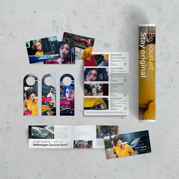 Verschiedene Volkswagen-Werbemittel wie Flyer, Türanhänger und Broschüren mit dem Slogan „Be yourself. Stay original.“ auf einem grauen Tisch ausgebreitet.