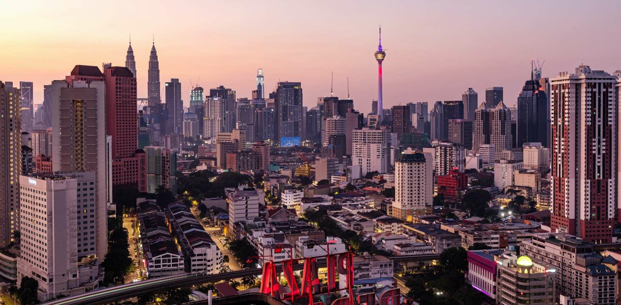 Panorama der Skyline von Kuala Lumpur bei Sonnenuntergang mit dem KL Tower und den Petronas Towers zwischen Hochhäusern.