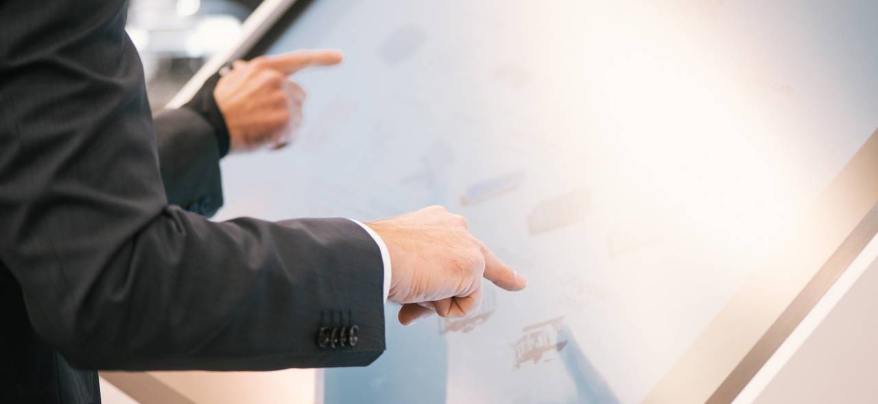 Zwei Personen in Anzügen bedienen gemeinsam einen großen Touchscreen.