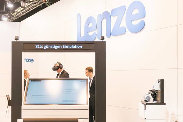 Drei Männer im Anzug, einer mit VR-Brille, an einer interaktiven Station mit dem Text „81 % günstiger: Simulation“.