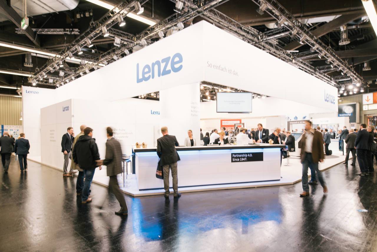 Großer, weiß leuchtender Messestand von Lenze auf Fachmesse, mit vielen Besuchern im Gespräch.