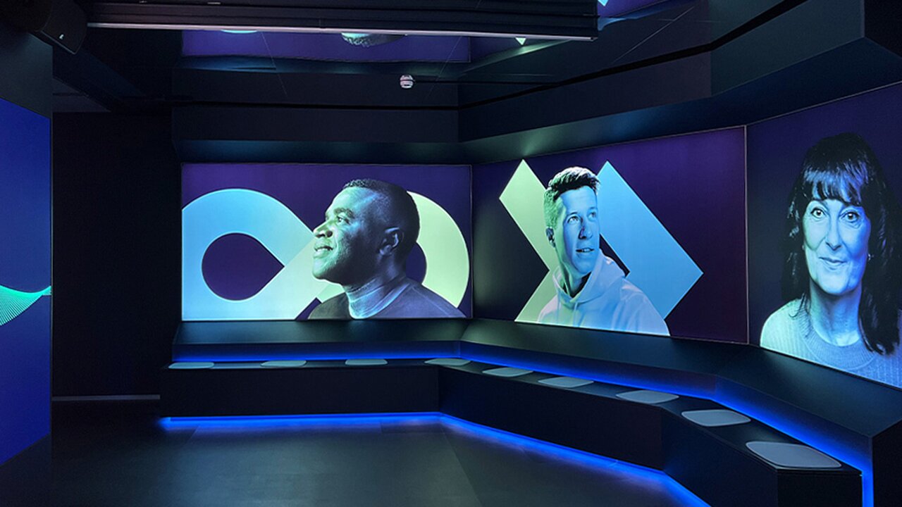 Dunkler Raum mit Panoramadisplays, die Porträts von Menschen in stilisierter Beleuchtung und grafischen Elementen zeigen.