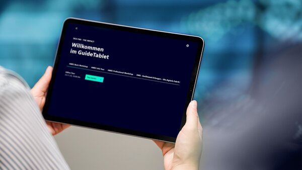 Nahaufnahme eines Tablets in Händen, das Bedienende im „GuideTablet“ willkommen heißt – mit Menü für Themenbereiche.