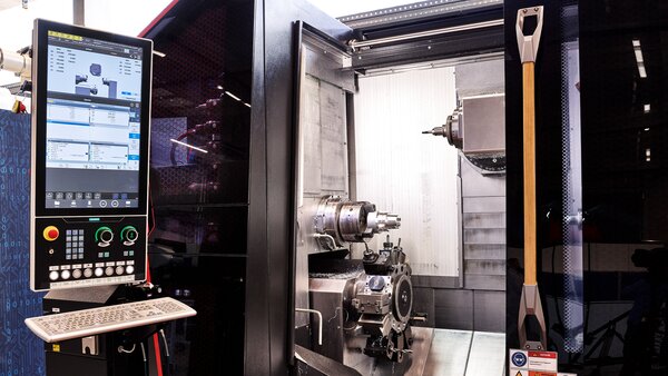 Industrielle CNC-Maschine mit geöffnetem Bearbeitungsraum und großem Bedienfeld mit Monitor und Steuerknöpfen.