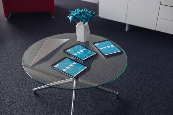 Runder Glastisch mit drei Tablets und moderner Vase mit blauer Papierblume.