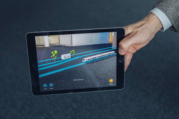 Tablet zeigt per Augmented Reality einen Zug, Schienen und Bäume auf dem Boden.