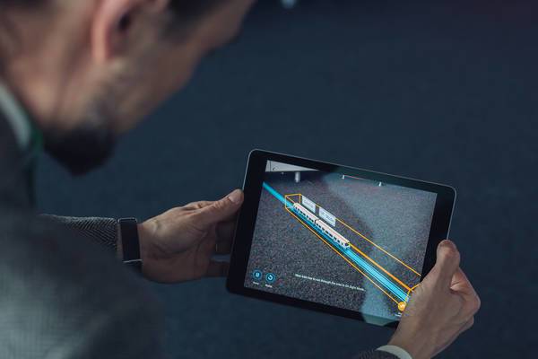 Mann betrachtet auf einem Tablet eine digitale Darstellung eines Zugs in Augmented Reality.