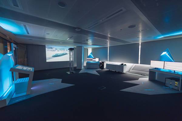 Modern ausgeleuchteter Raum mit Touch-Displays, Beamern und Steuerpulten.