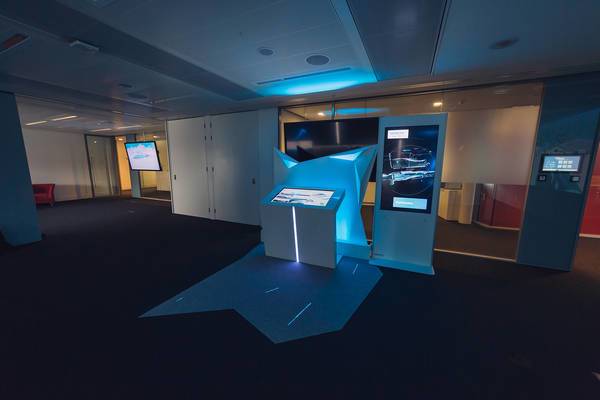 Ausgeleuchtete Präsentationsstation mit Touchscreen und Infodisplay in dunklem Raum.