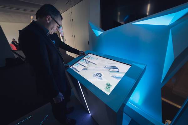 Mann bedient einen interaktiven, beleuchteten Präsentationstisch mit Touchscreen im Dunkelraum.