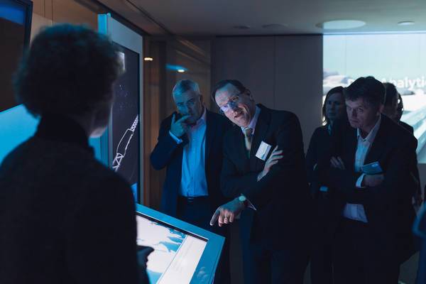 Mehrere Personen betrachten gemeinsam eine interaktive Bildschirmpräsentation in dunklem Raum.