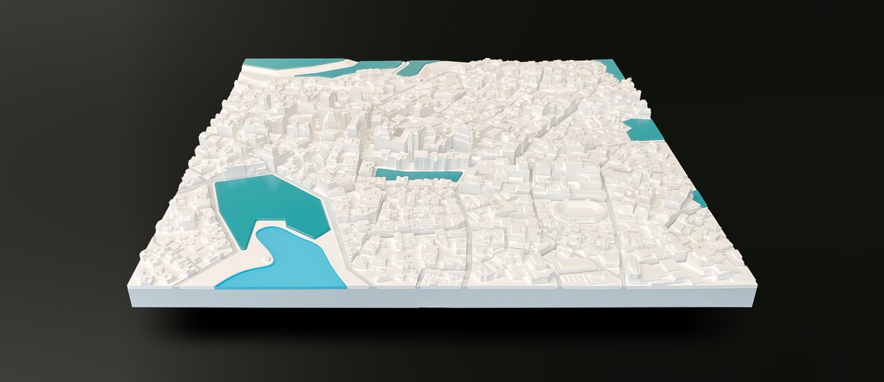 Detailliertes physisches Stadtmodell in Weiß mit hervorgehobenen Wasserflächen in Blau – perspektivisch von schräg oben fotografiert.