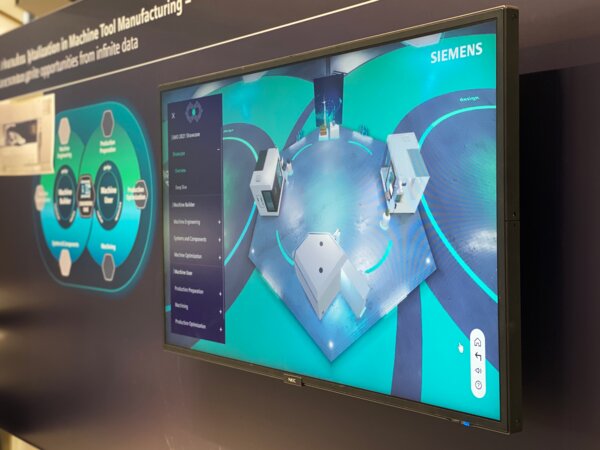 Bildschirm mit Draufsicht einer virtuellen Produktionshalle, inklusive Maschinen und Bedienfeldern im Siemens-Design.