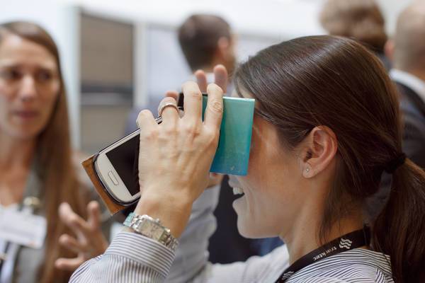 Frau mit Smartphone in Papp-VR-Brille bei einer Produktpräsentation.