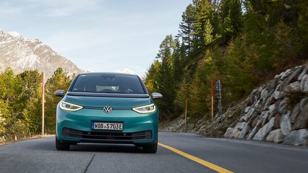 Ein türkises Volkswagen-Elektroauto fährt auf einer Landstraße durch eine bergige Landschaft.